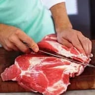 En person skär en bit kött på en skärbräda.