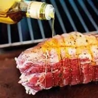 En bit kött med rutnät på ytan får olja hälld över sig från en flaska.