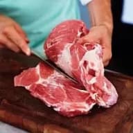 En person skär i ett stort stycke kött på en skärbräda.