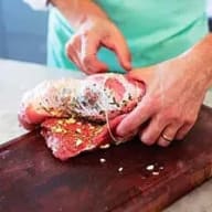 En person skär i ett stycke kött på en skärbräda.