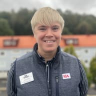 En ICA-anställd står utomhus i väst med namnbricka.