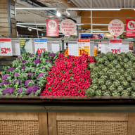 Rader av grönsaker och frukt uppställda i en mataffär med synliga prisskyltar.