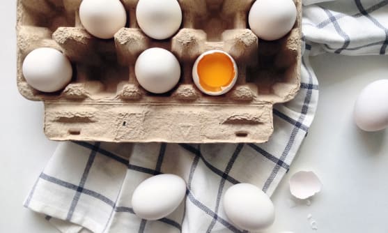 En öppen äggkartong med hela och knäckta ägg ligger på en rutig kökshandduk.