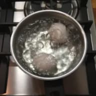 En kastrull med kokande vatten och några ägg på en spis.