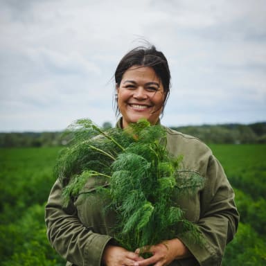 En person håller en stor bukett dill i ett fält.