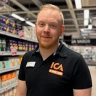 En ICA-medarbetare i butikskläder står i en butiksgång.