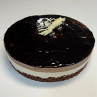 En rund flerlagrad chokladtårta med glasyr och chokladdekoration på toppen.