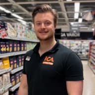 En ICA-medarbetare i butikskläder står i en butiksgång.