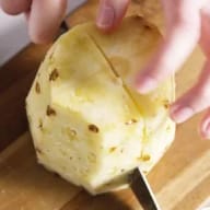 En person skär en ananas på en skärbräda.