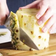 En person skär en bit ananas med en kniv på en skärbräda.