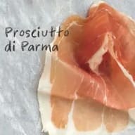 En skiva prosciutto di Parma ligger på ett underlag.