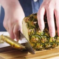 En person skär en ananas på en skärbräda med en kniv.