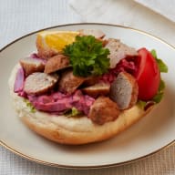 Öppen macka med skivade köttbullar på krämig sallad, garnerad med persilja och tomat.