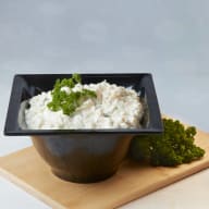 Skål med krämig sallad toppad med persilja på en skärbräda.