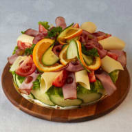 Smörgåstårta toppad med skivat kallskuret, ost, grönsaker och fruktskivor.