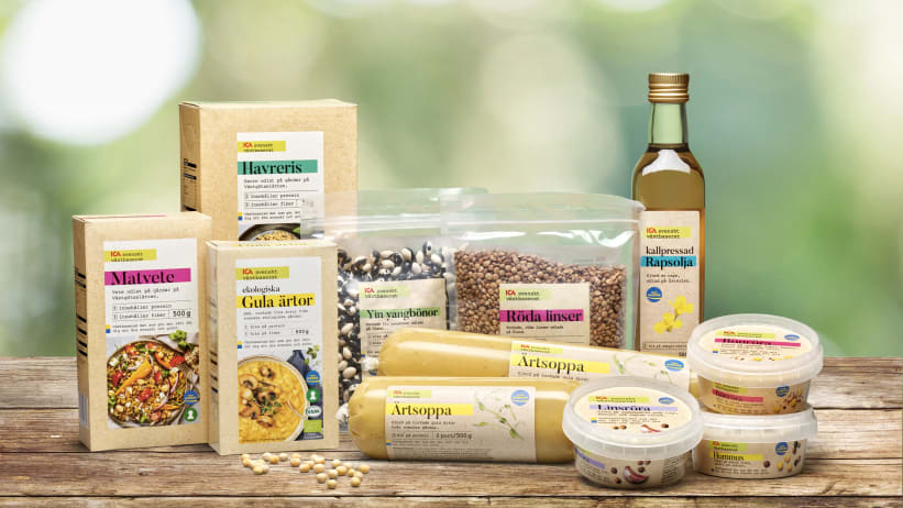 Produkter ur sortimentet ICA svenskt växtbaserat står på ett träbord med grönskande bakgrund