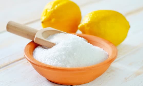 En skål med ett vitt pulver som nog är citronsyra och två färska citroner bredvid.