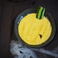 En skål med gul hummus och ett gurkskaft.