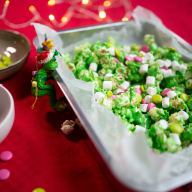 En tallrik med broccoli och små marshmallows står på ett bord bredvid en skål och en julfigur.