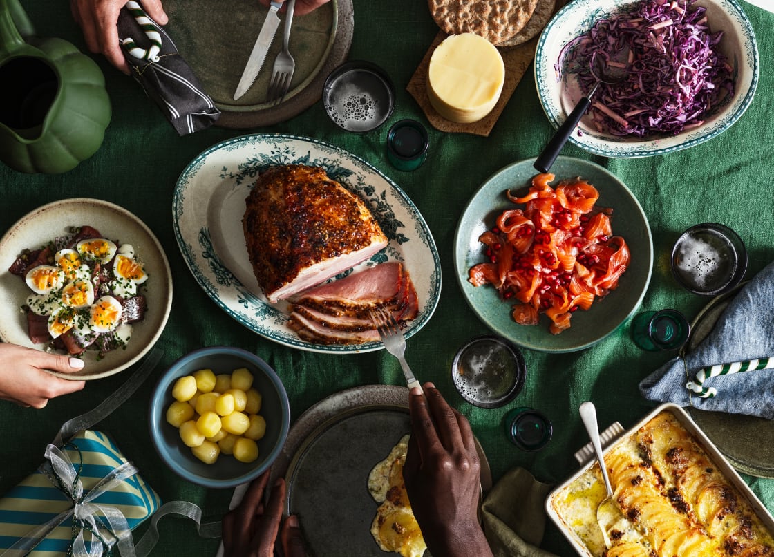 En person skär upp en glaserad skinka på ett dukat bord med olika rätter.