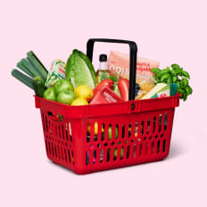 Rosa bakgrund, röd kundkorg fylld med matvaror.