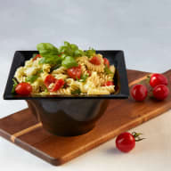 Skål med pastasallad med fusilli, örter och tomater på ett skärbräde.