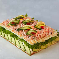 En smörgåstårta dekorerad med räkor, ägg och gurkskivor.