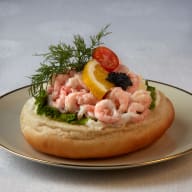 Öppen smörgås toppad med räkor, salladsblad, citronklyfta, dill och rom på en tallrik.