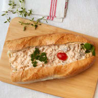 Baguette fylld med krämig salladsfyllning, garnerad med persilja och en körsbärstomat.