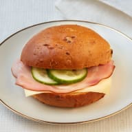 Smörgås med skinka, ost och gurkskivor på en tallrik.