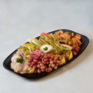 Stort serveringsfat med skivad kallskuret, vindruvor, skivad frukt och en skål dip.