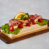 Smörgåstårta med salladsblad, skivat pålägg, rullad ost och grönsaksdekoration på en träbricka.