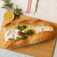 Baguette fylld med räksallad, dill och en citronskiva på en skärbräda.