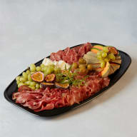 Ett serveringsfat med skivat charkuterier, ost och uppskuren frukt.