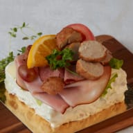 Smörgåstårta toppad med skinka, skivade korvbitar, apelsinklyfta och persilja.