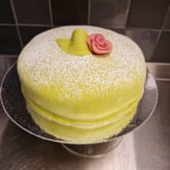 En rund prinsesstårta på fat med en marsipanros och ett blad på toppen.