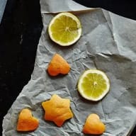 Torkade apelsinskivor och utstansade stjärnor av apelsinskal på en ugnsplåt med bakplåtspapper.