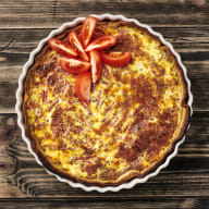 En paj i pajform toppad med skivade tomater på ett träbord.