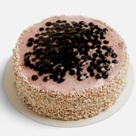 Rund tårta toppad med blåbär och täckt runtom med hackade nötter på ett serveringsunderlägg.