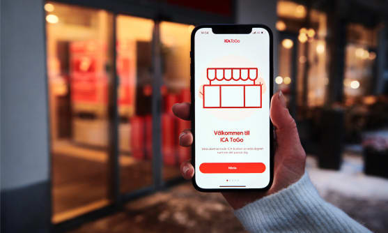 En ICA-butik i kvällsljus. En hand håller upp en mobil där det står 