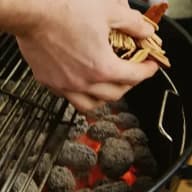 En person håller en tändare över glödande kol i en grill.