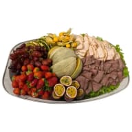 Serveringsbricka med melonhalvor, bär, passionsfrukt och skivat kallskuret.