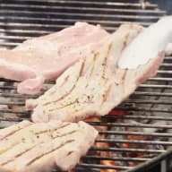 Köttstycken ligger på ett grillgaller över glödande kol.