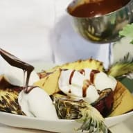 En tallrik med ananasskivor, glass och chokladsås serveras bredvid en skål med mer sås.