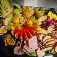 Serveringsfat med upplagd frukt och skivat kallskuret kött.