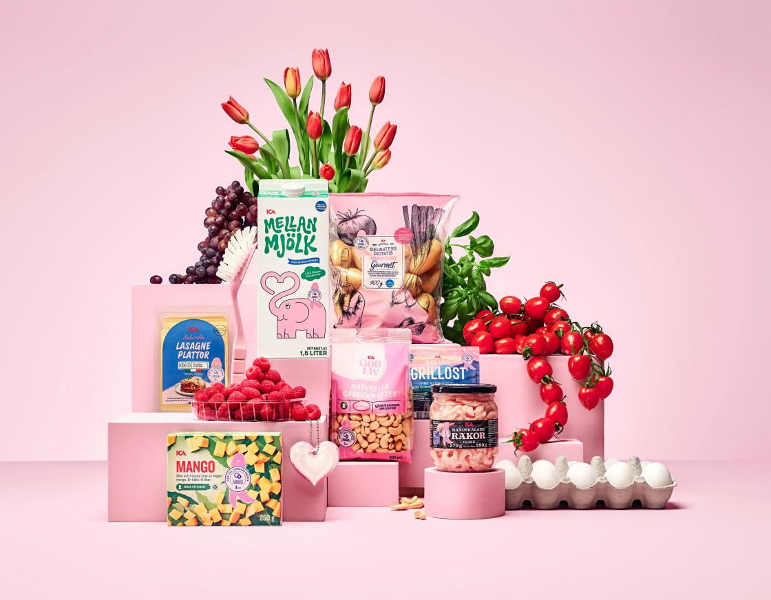 En samling matvaror, blommor och ägg står placerade på ett podium framför en vägg.