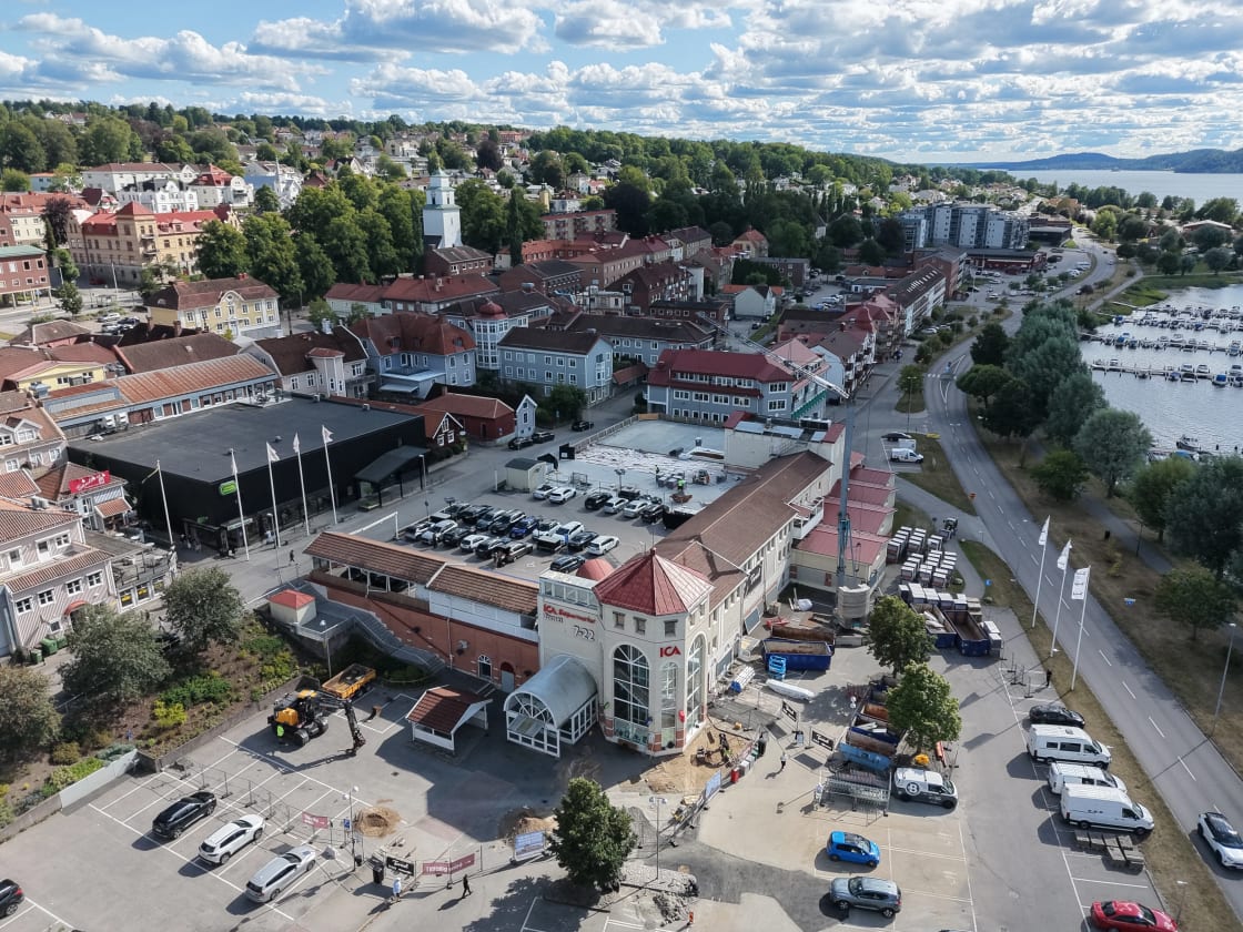 Flygfoto över stadens centrum med en ICA-butik, parkeringsplats och småbåtshamn vid vattnet.