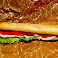 Baguettesmörgås fylld med kalkon, salladsblad, och tomat liggande på veckat papper.