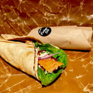 En fylld wrap med varmrökt lax, sallad och skivade grönsaker mot en pappersbakgrund
