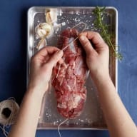 En person binder ett stycke kött med snöre på en metallbricka.